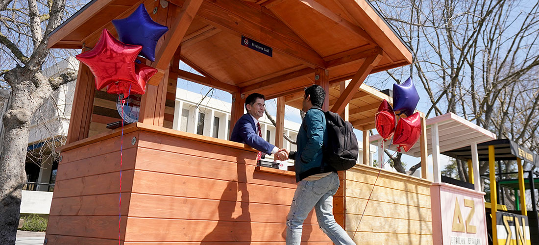 President Saúl shakes hands with a student at the connection booth